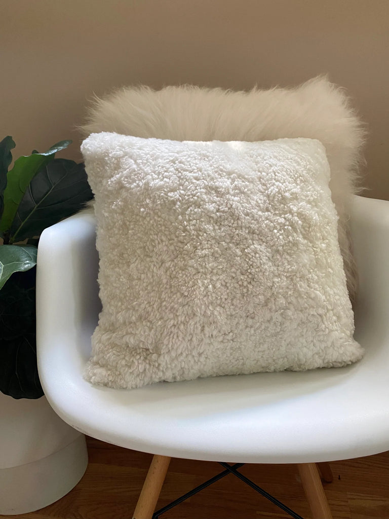Iivory shearling sheepskin pillow on a white chair 
