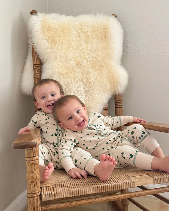 Two children in matching outfits sitting on a wooden chair with a bright ivory nursery sheepskin