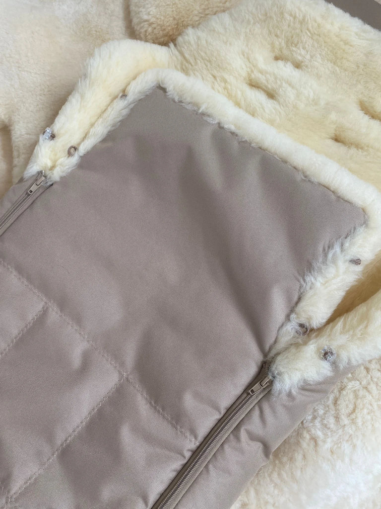 baby and toddler sleeping bag with cream sheepskin lining placed on a fluffy rug