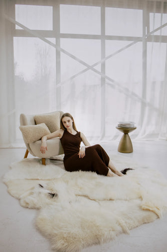 Woman sitting on mixed textured sheepskin rug in a modern room with large windows