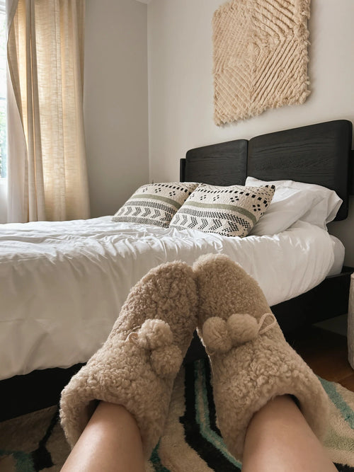 Person wearing organic sheepskin slippers in a bedroom 