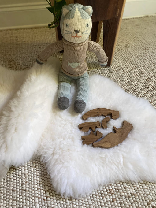 Knitted cat toy with wooden pieces on small white nursery pelt