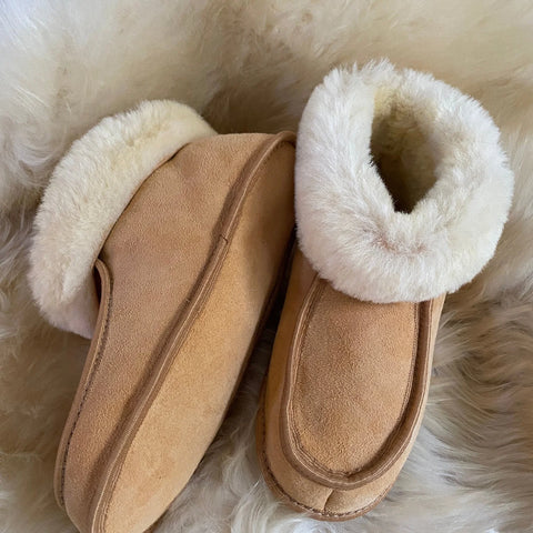 Pair of tan suede slippers with white sheepskin lining on a fluffy cream surface