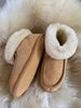 Pair of tan suede slippers with white sheepskin lining on a fluffy cream surface
