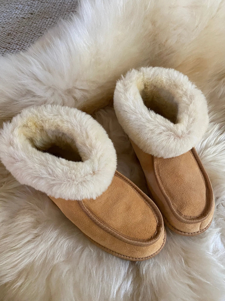 Pair of tan suede slippers with white sheepskin lining on a fluffy cream surface
