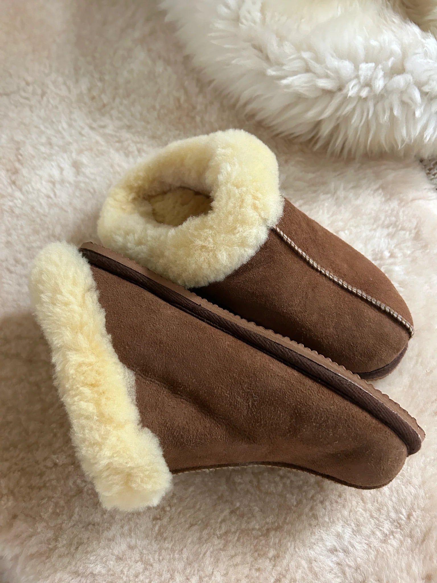 The cottage slipper with cream fur lining on a soft, beige surface