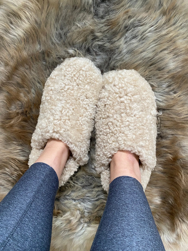 The everyday slip on tan shearling sheepskin worn on a fluffy brown rug