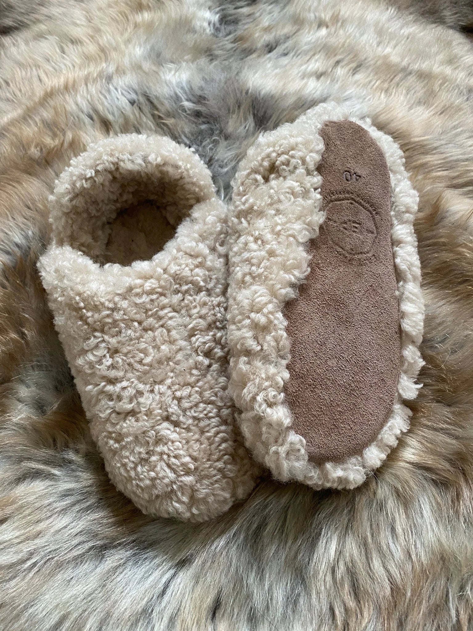 Pair of the everyday slip on tan shearling sheepskin on a fluffy fur surface